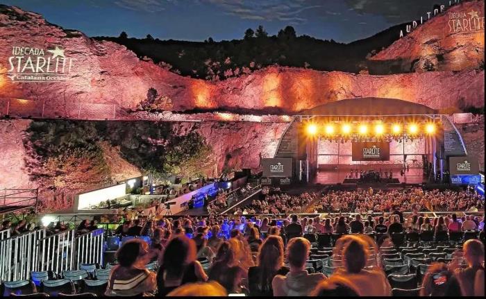 cantera con escenario musical incrustado y personal sentadas en una grada de noche